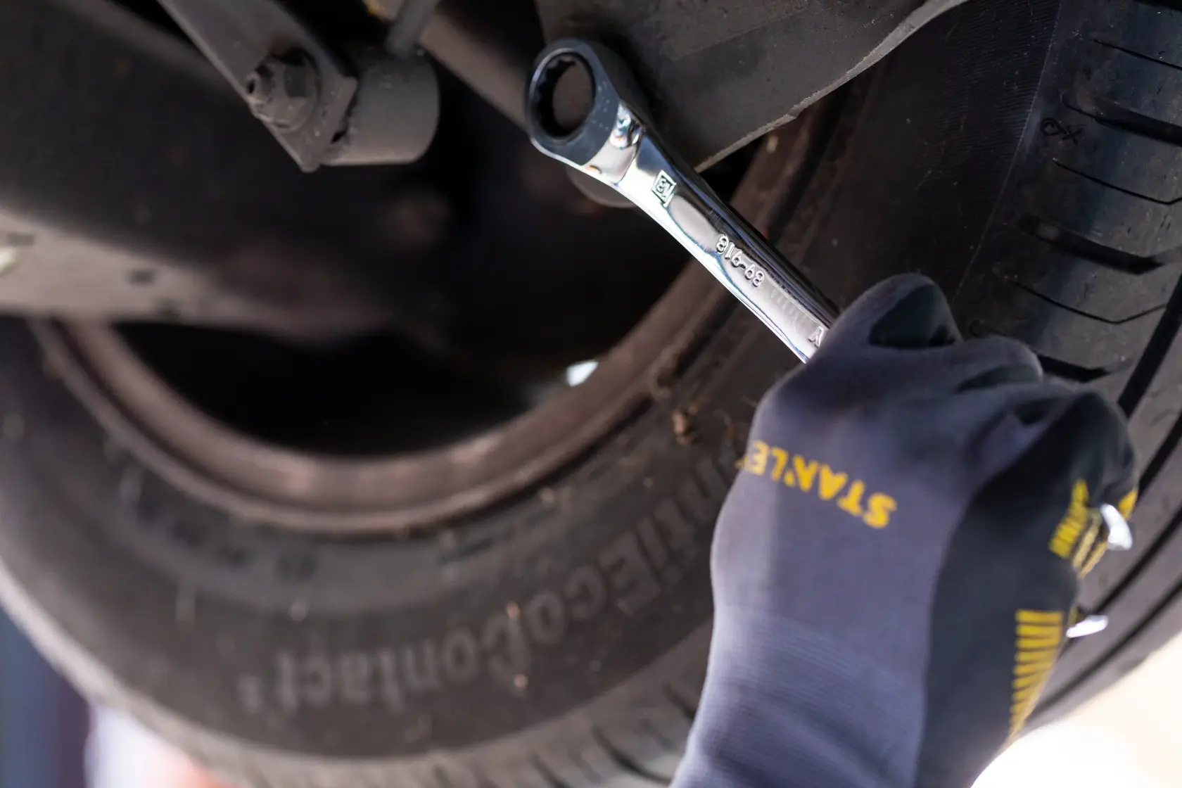 STANLEY STMT89910-0 Schraubenschlüssel in Benutzung am Auto-Unterboden, Bediener trägt STANLEY Handschuhe, Nahaufnahme.