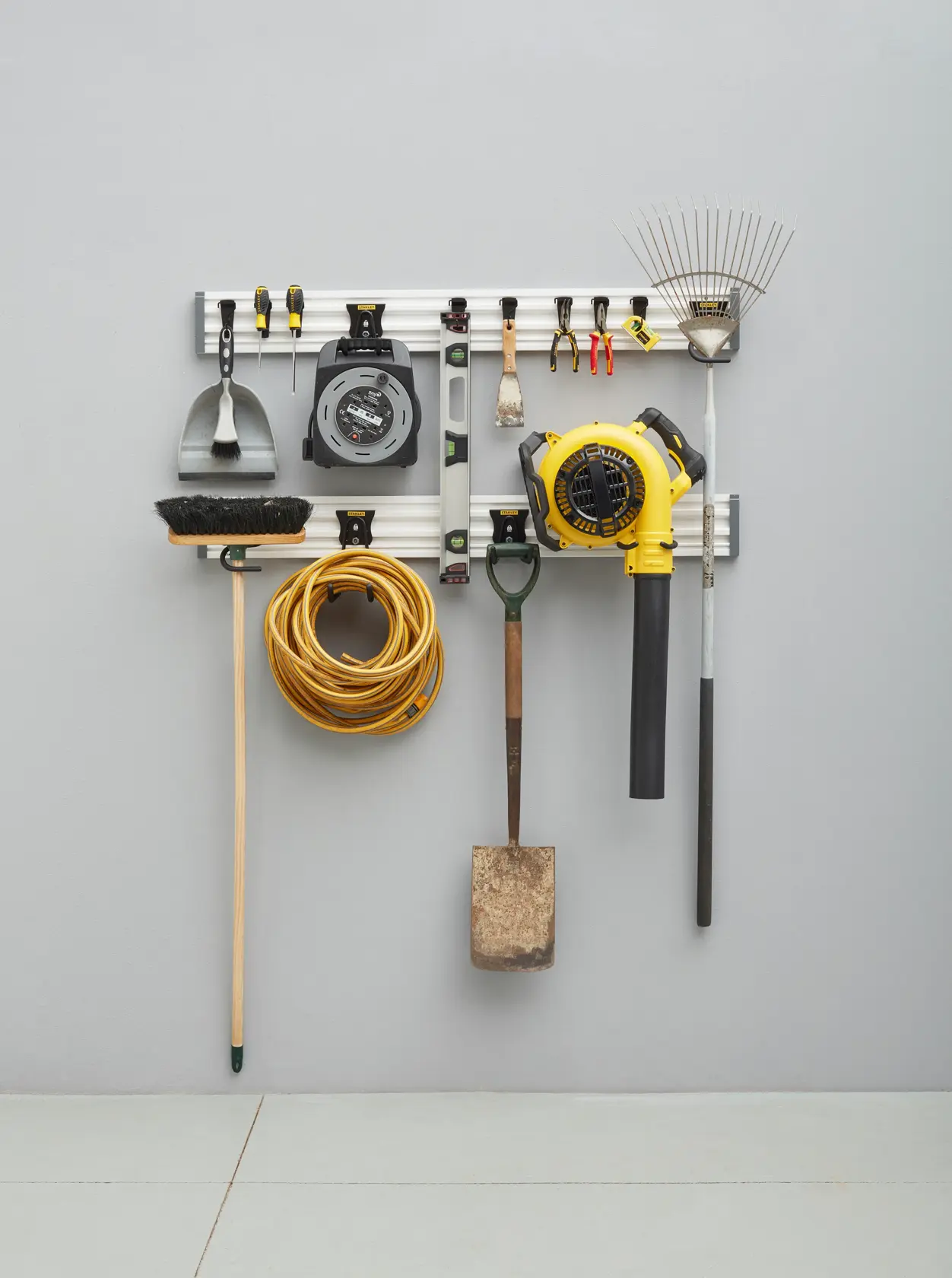 STANLEY STST22000-1 Wand-Organizer-Schiene mit verschiedenen Werkzeugen wie Rechen, Laubbläser, Besen, Kabel und Handwerkzeugen.