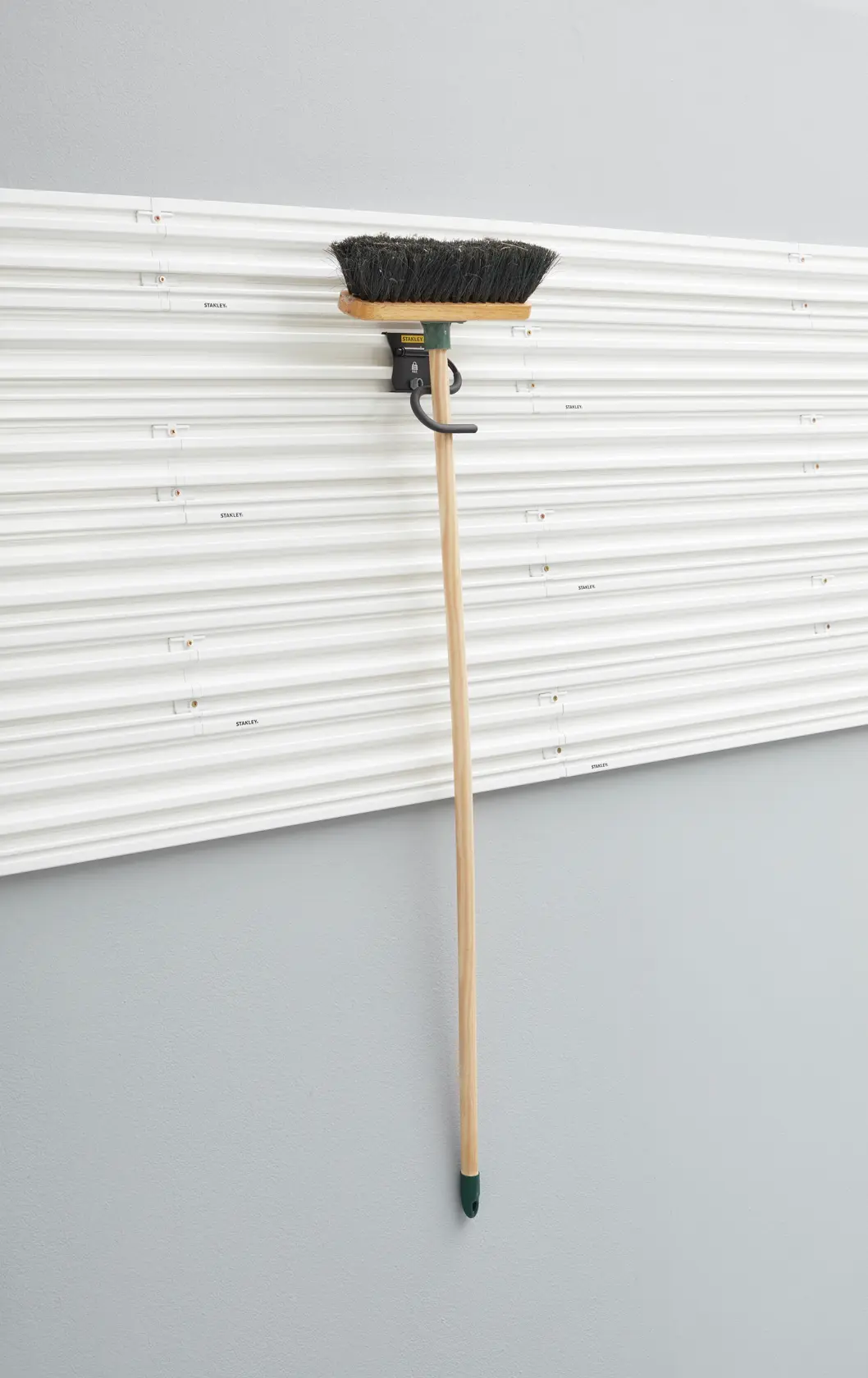 Foto des STANLEY STST82605-1 Wandaufbewahrungshakens mit Besen an einer weißen Lamellenwand.