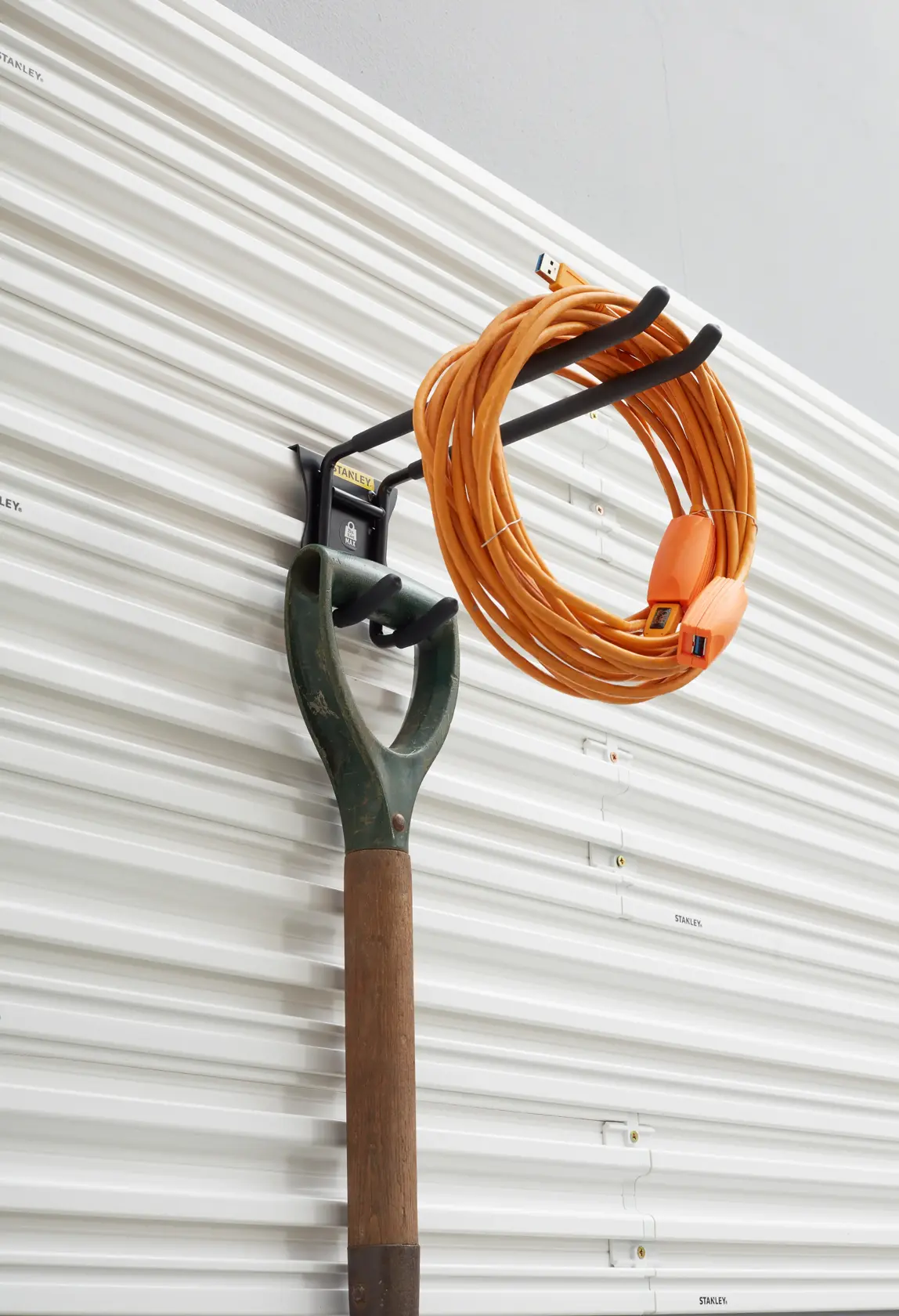 STANLEY STST82606-1 Wandhaken mit Gartengerät und orangefarbener Verlängerungsschnur, Seitenansicht.