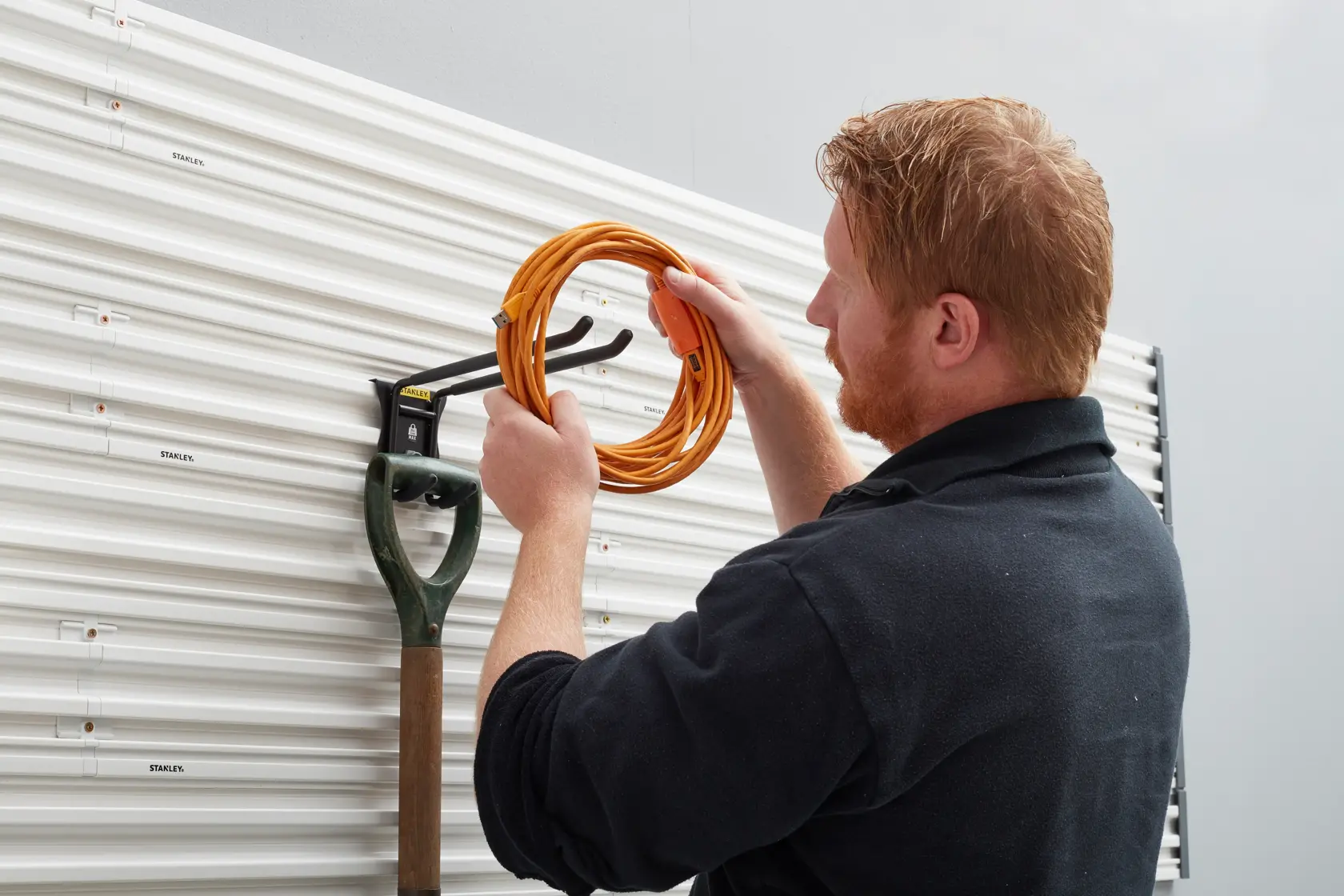 STANLEY STST82606-1 Wandorganizer mit Haken, hält eine Schaufel und ein orangefarbenes Verlängerungskabel.