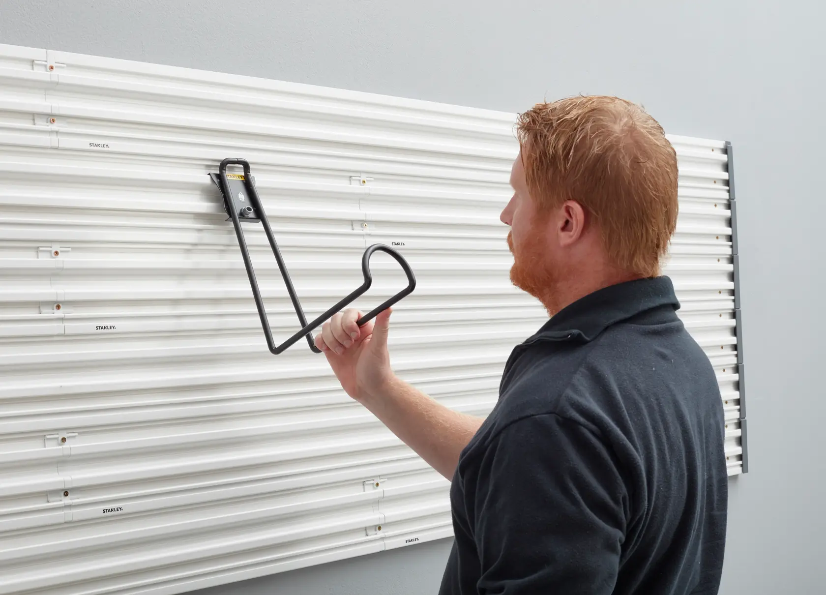 Person befestigt STANLEY STST82614-1 Wandhaken an weißem Wandpaneelsystem, Seitenansicht.
