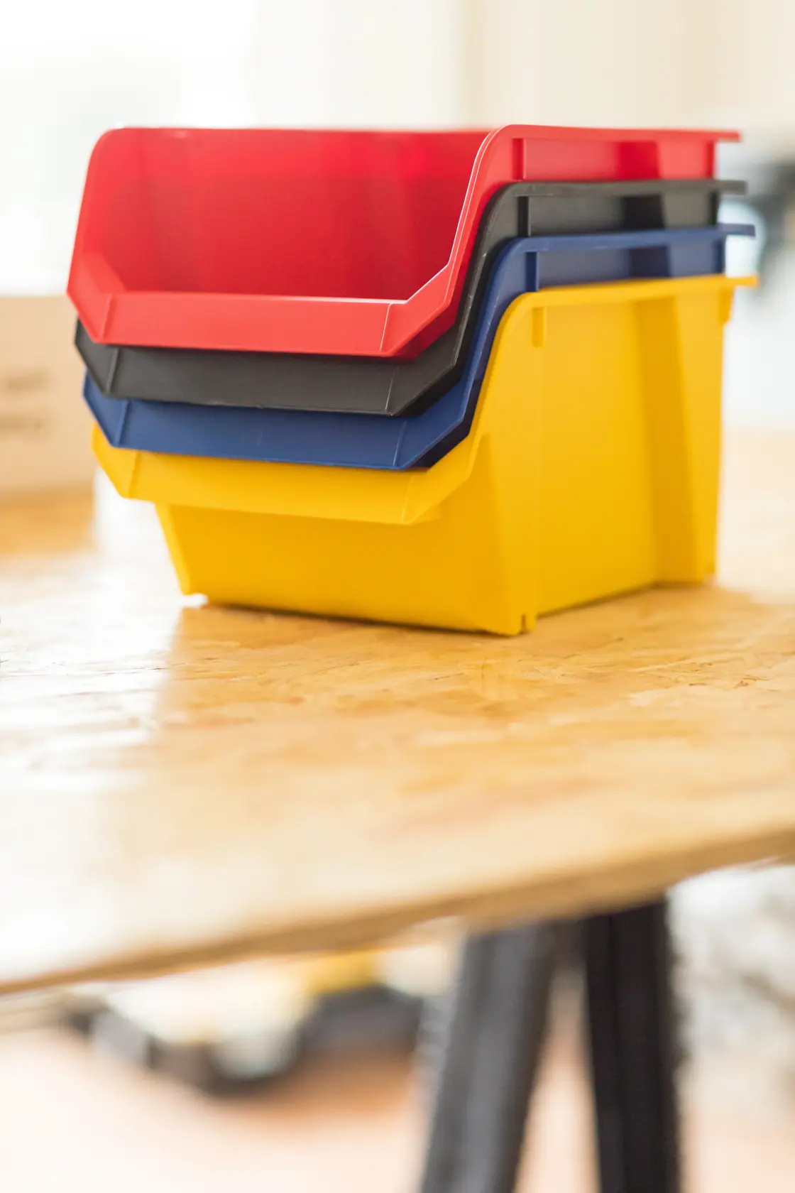 STANLEY STST82739-1 stapelbare Kunststoffboxen in Rot, Schwarz, Blau und Gelb auf Holztisch, Seitenansicht.