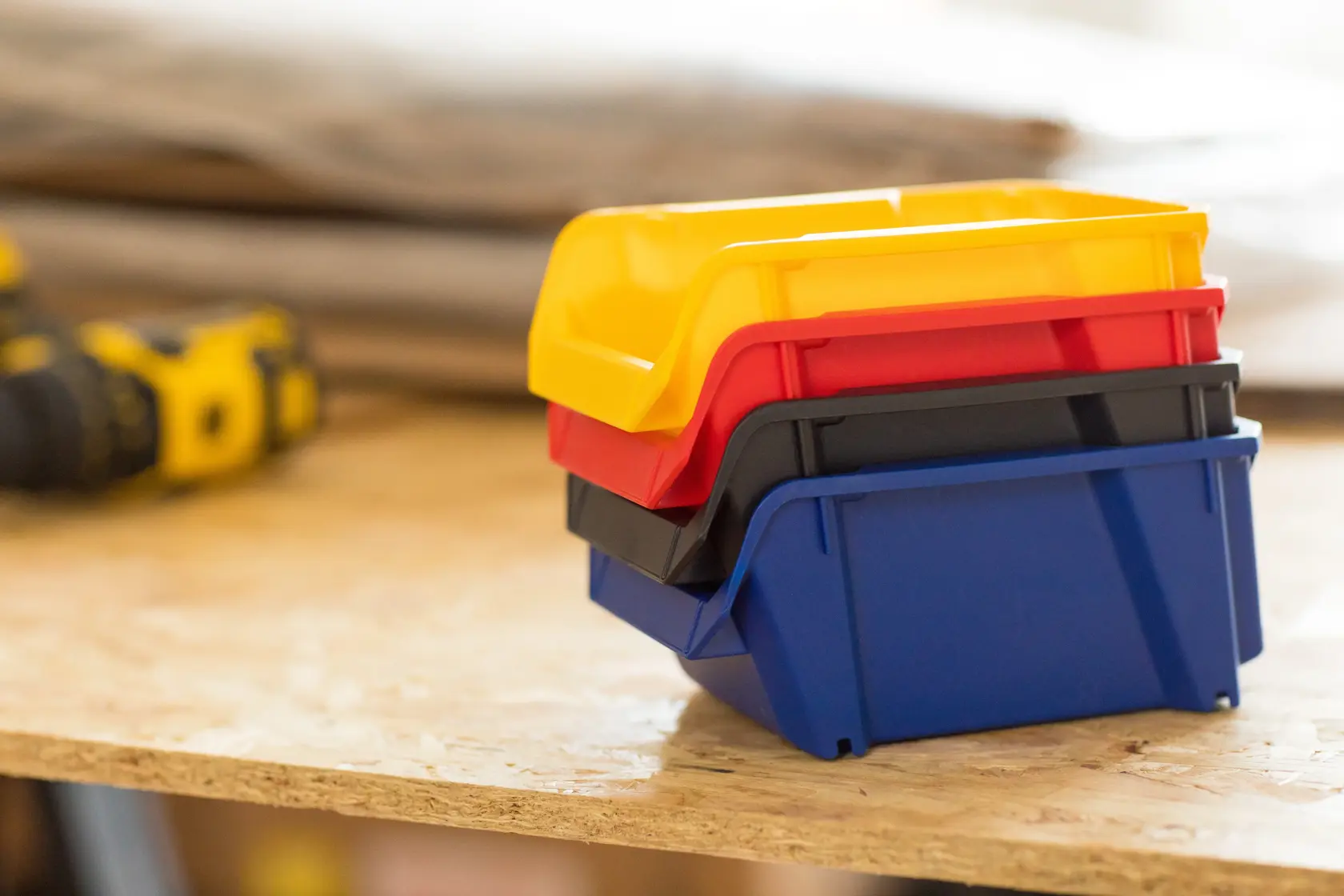 STANLEY STST82740-1 stapelbare Kunststoffboxen in Gelb, Rot, Schwarz, Blau auf Werkbank, Seitenansicht.
