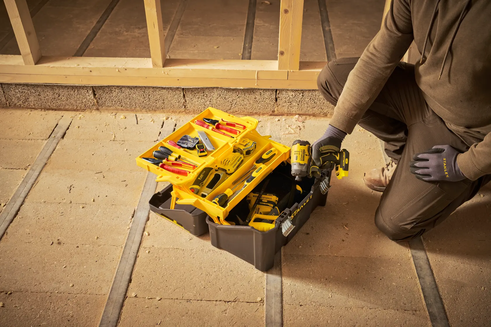 STANLEY STST83397-1 Werkzeugkasten offen mit verschiedenen Werkzeugen und Bohrmaschine auf Baustelle.