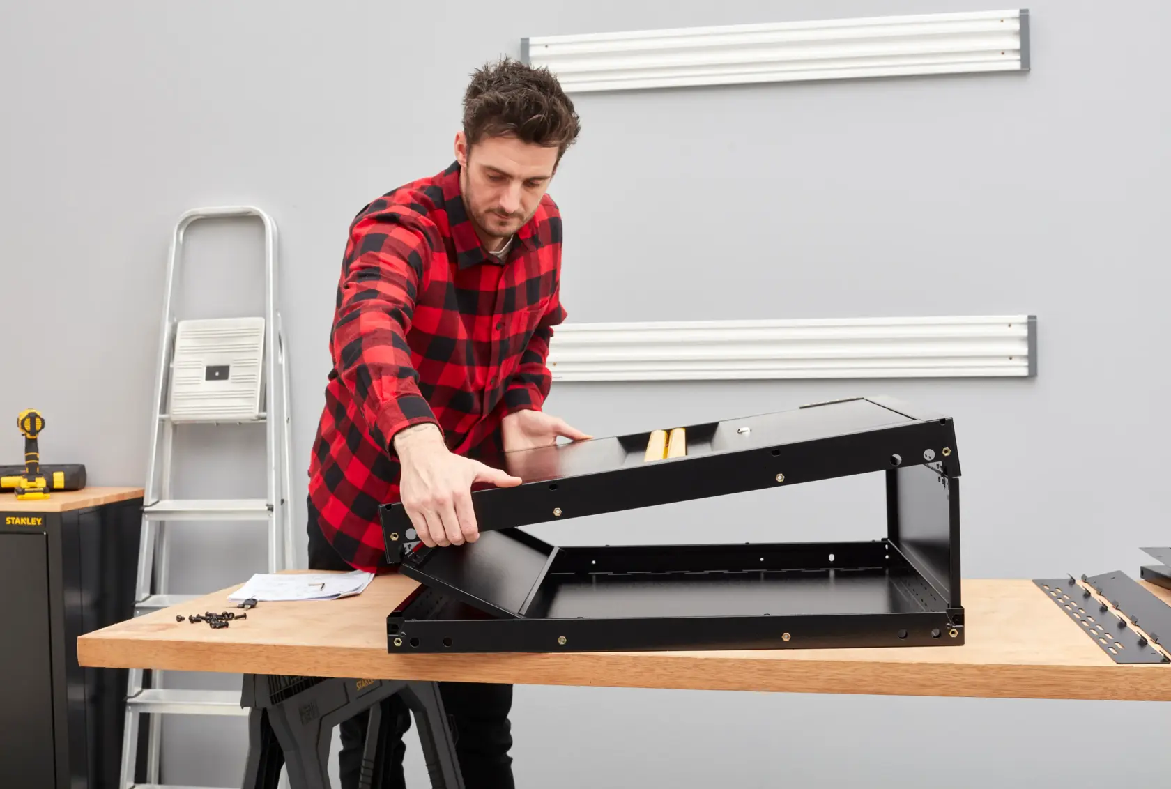 Person baut ein schwarzes STANLEY-Fotografie-Zubehör auf einer Werkbank im Atelier zusammen.