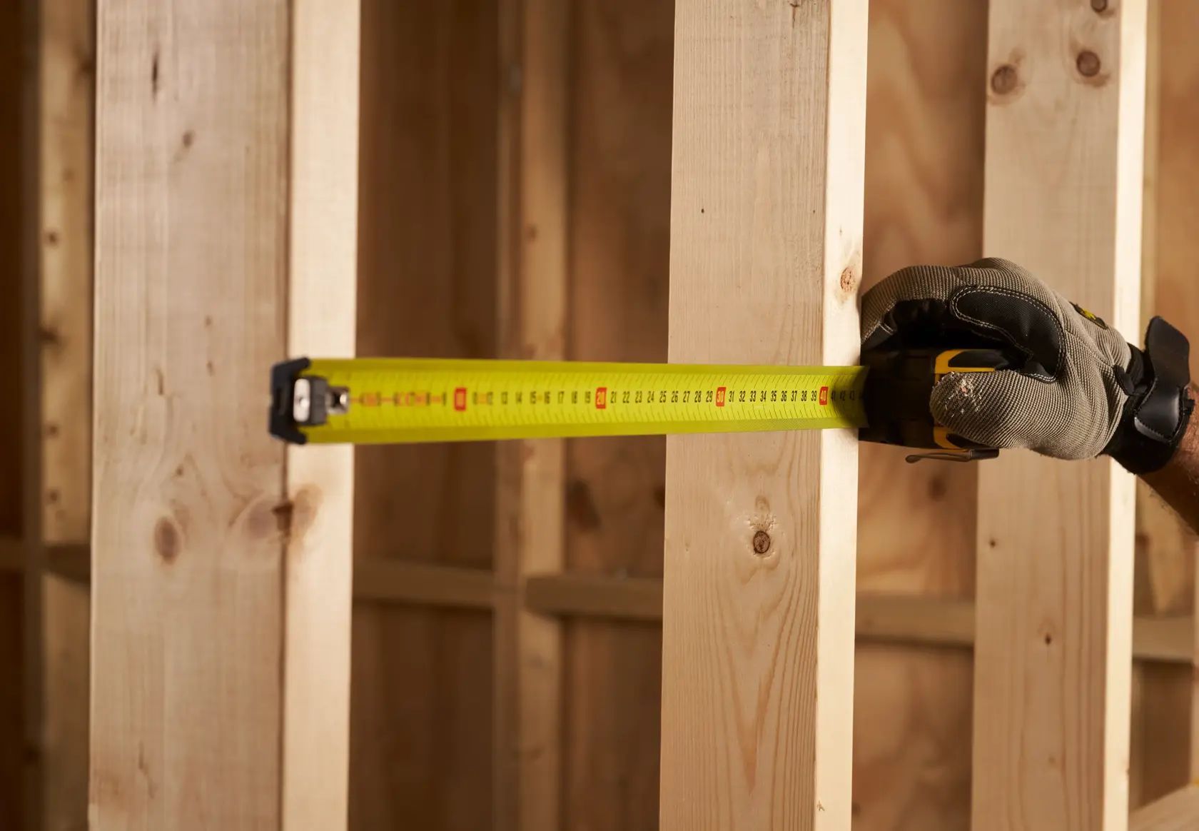 STANLEY XTHT0-33671 Maßband ausgezogen, misst Holzständer mit behandschuhter Hand auf Baustelle.